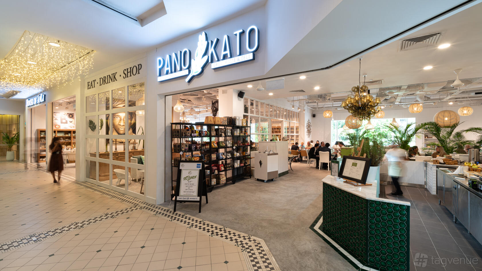 A restaurant with an open entrance, glass partitions, lush greenery, and a wall of books at Pano Kato by House of AnLi.
