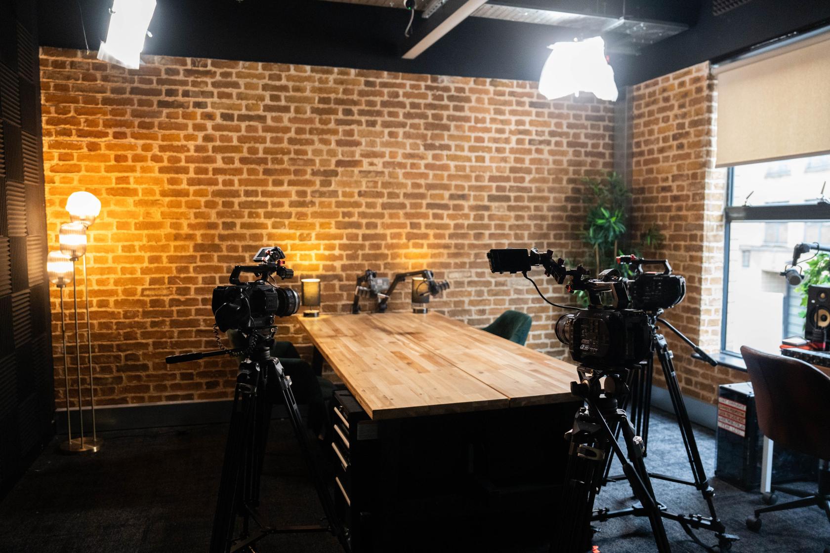 A film studio with exposed brick walls, a large wooden table, and video cameras set up at EC1 Campus.