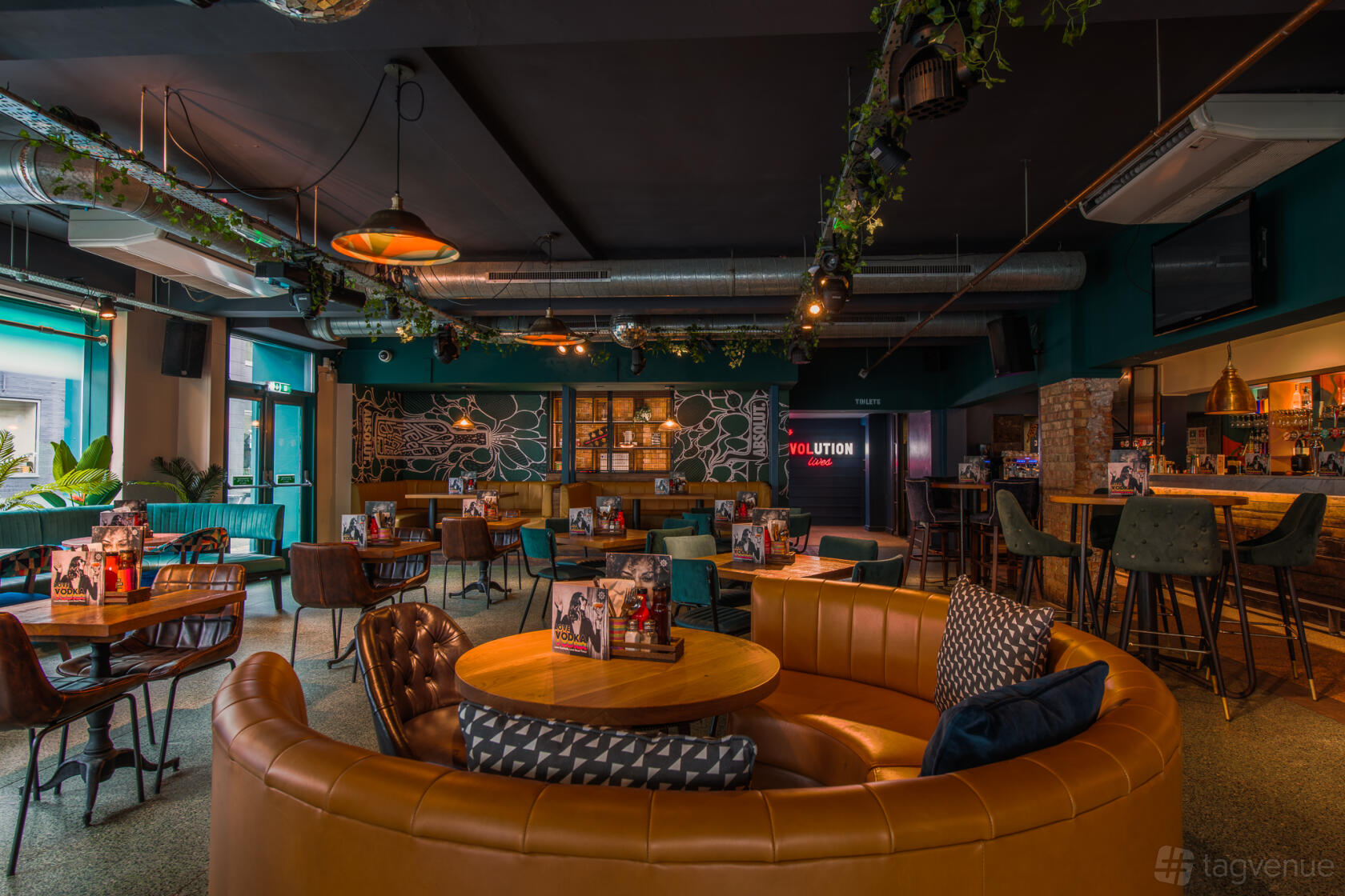 A bar with leather banquettes, wooden tables, exposed ductwork, and neon signage at Revolution Southampton.