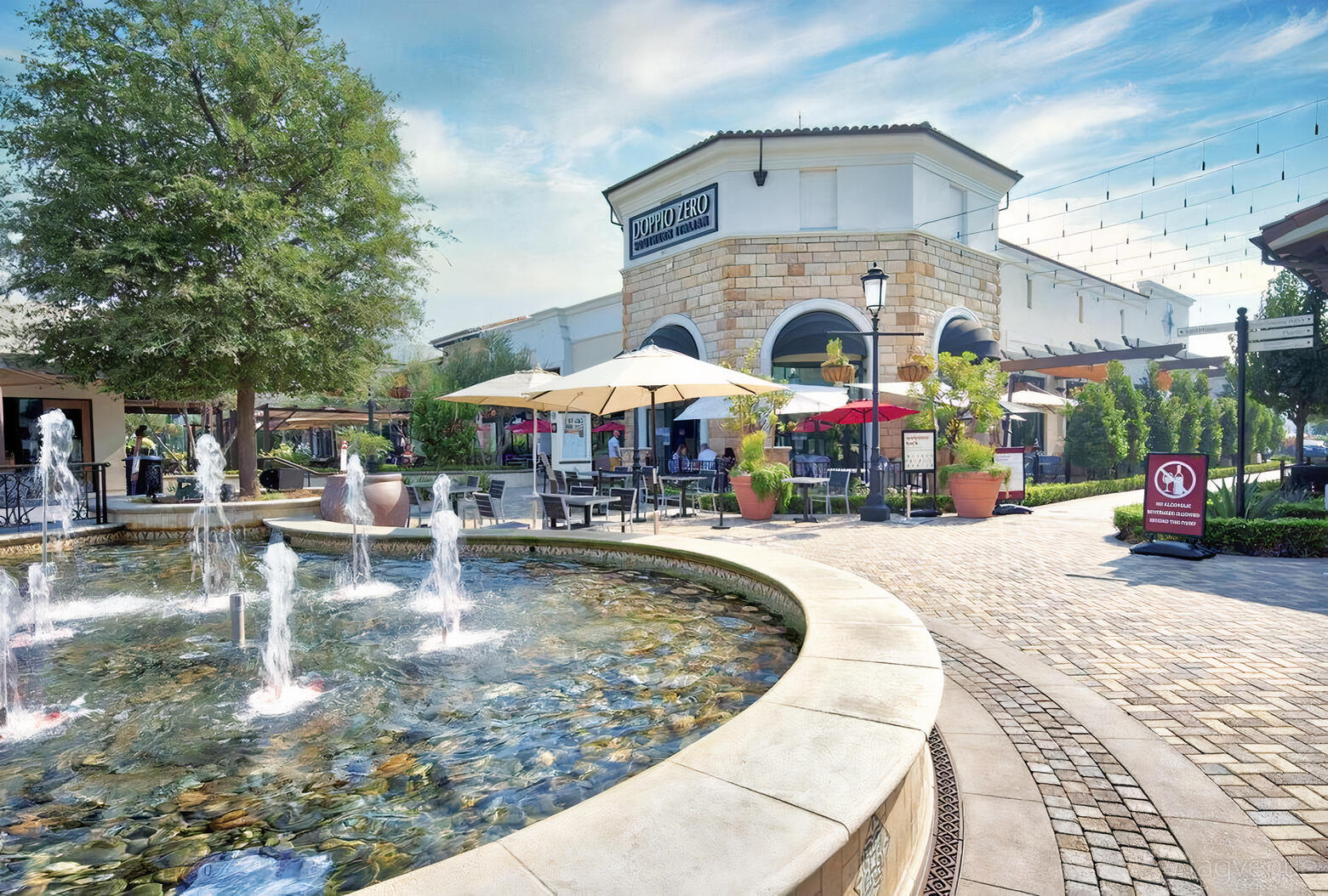 A restaurant with an outdoor patio, round tables shaded by umbrellas, and a stone fountain at Doppio Zero Concord.