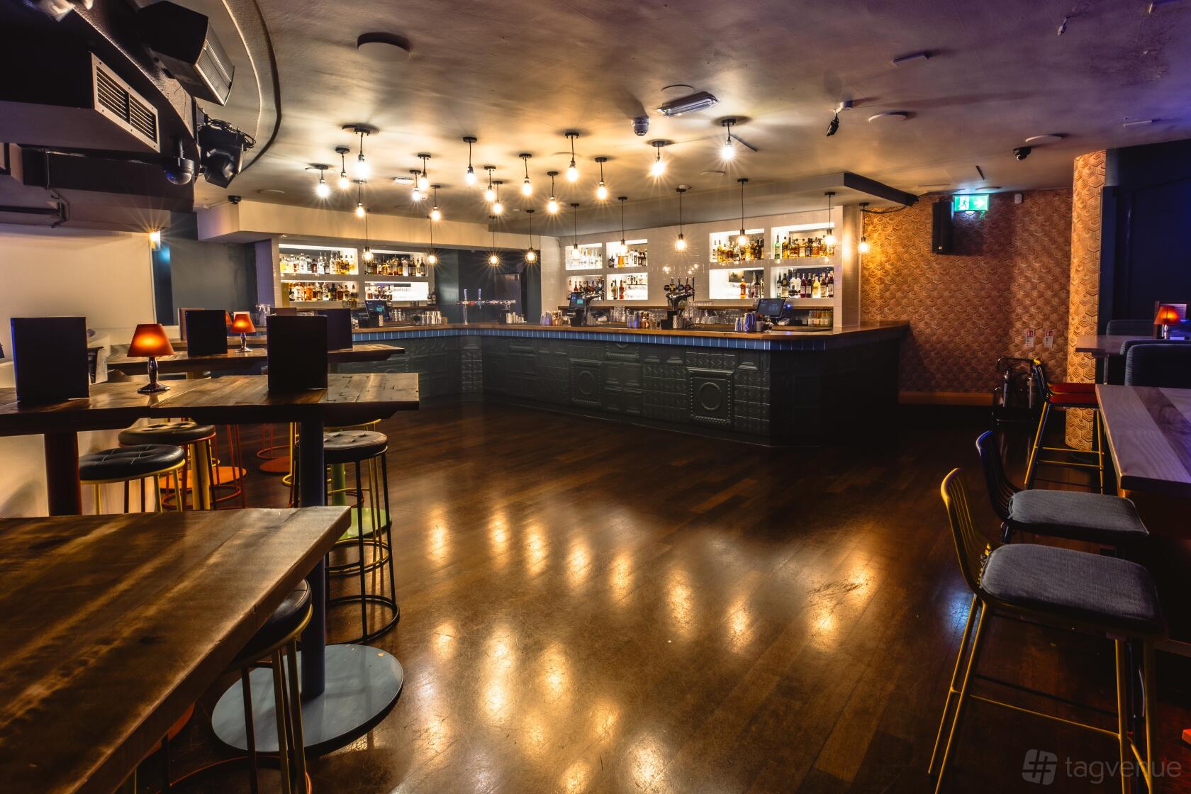 An event venue with a spacious wooden floor, high tables, bar seating, and pendant lighting at The Piano Works Covent Garden.
