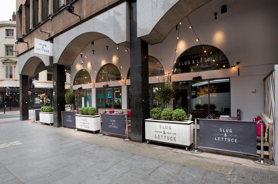 An outdoor pub area with arched windows, string lights, and branded planters at Slug and Lettuce Liverpool.