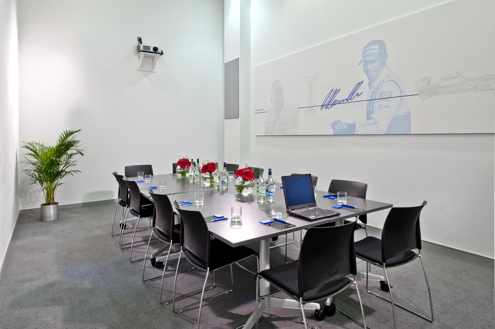 A meeting room with a boardroom table, black chairs, glass bottles, and motorsport-themed wall art at Mercedes-Benz World.