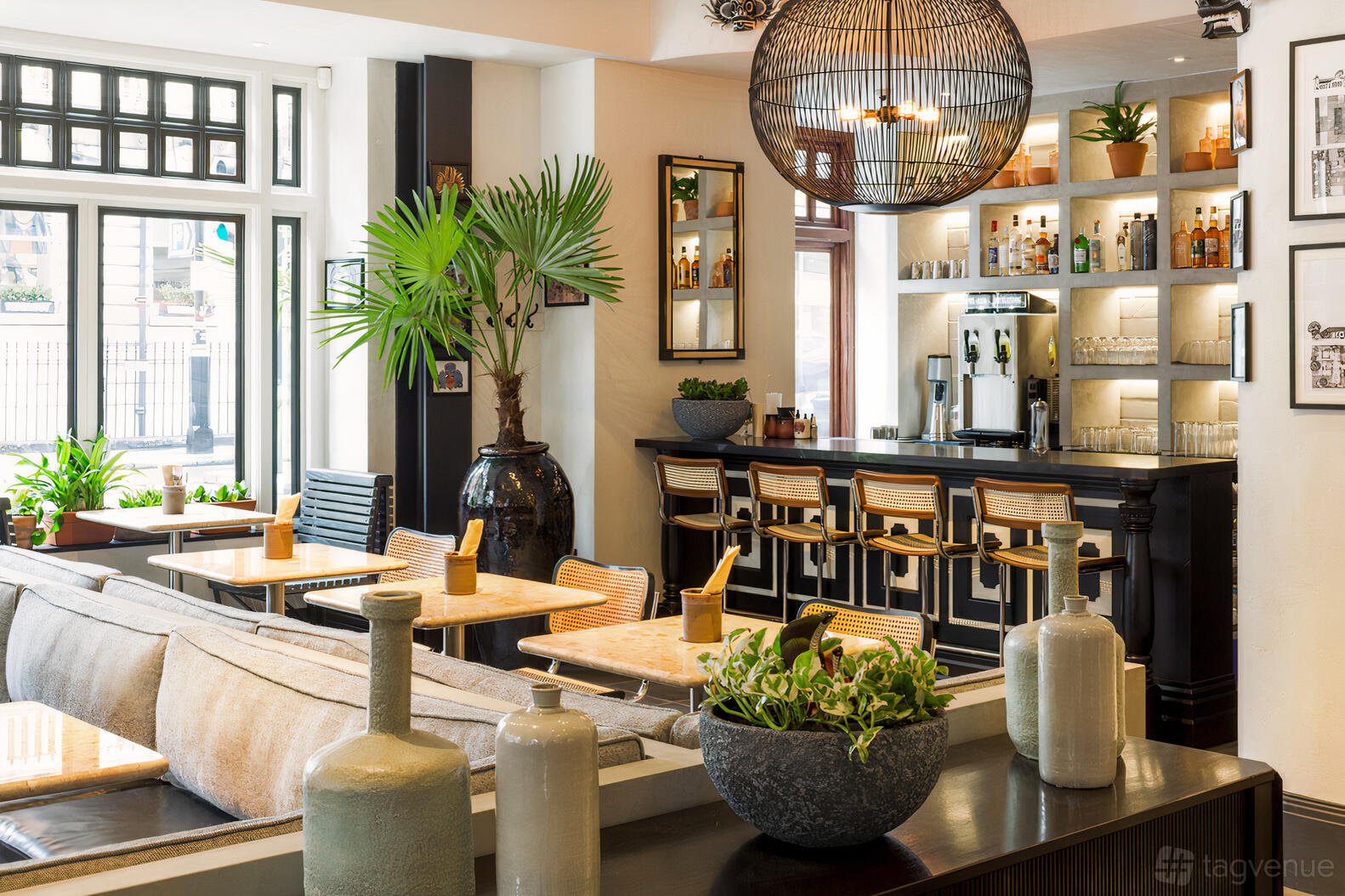 A restaurant with wooden tables, cushioned bench seating, potted plants, and a backlit bar at Hoppers Marylebone.