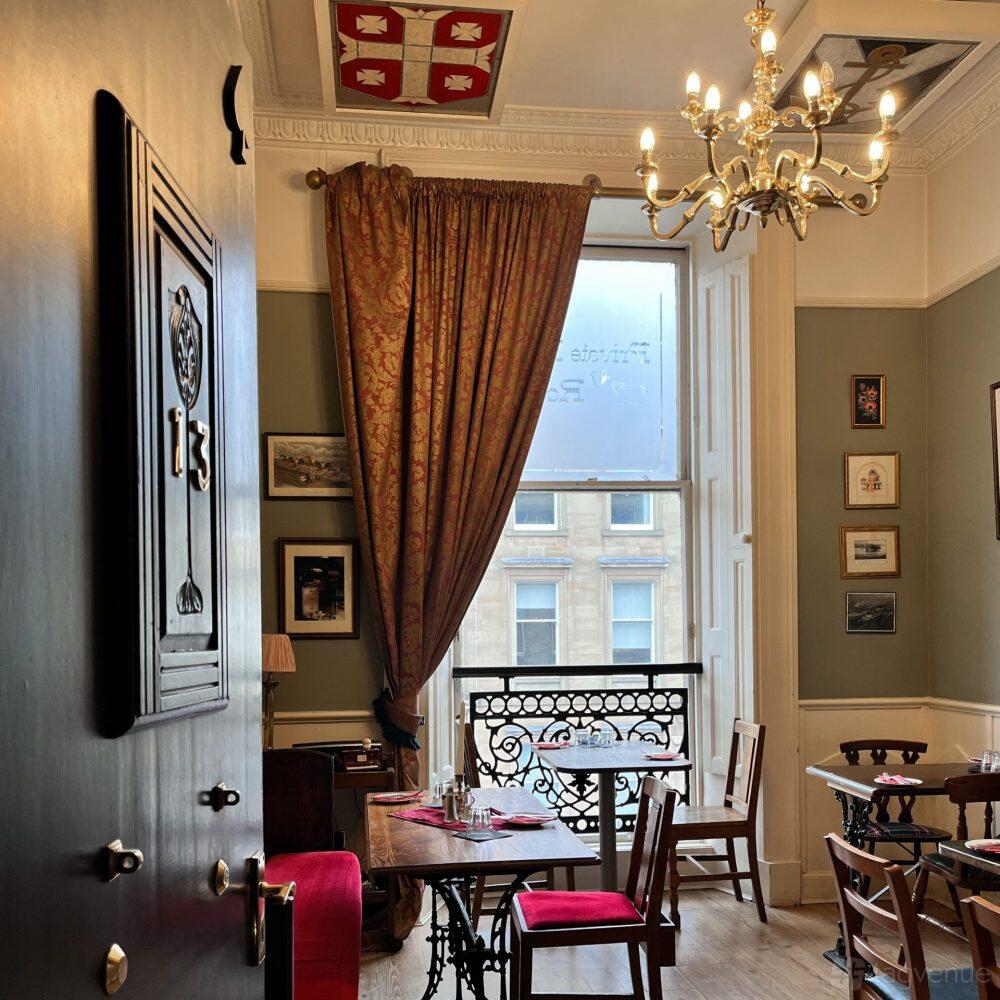 A dining room with high ceilings, large window with patterned drapes, and wooden tables at The Butterfly and The Pig.