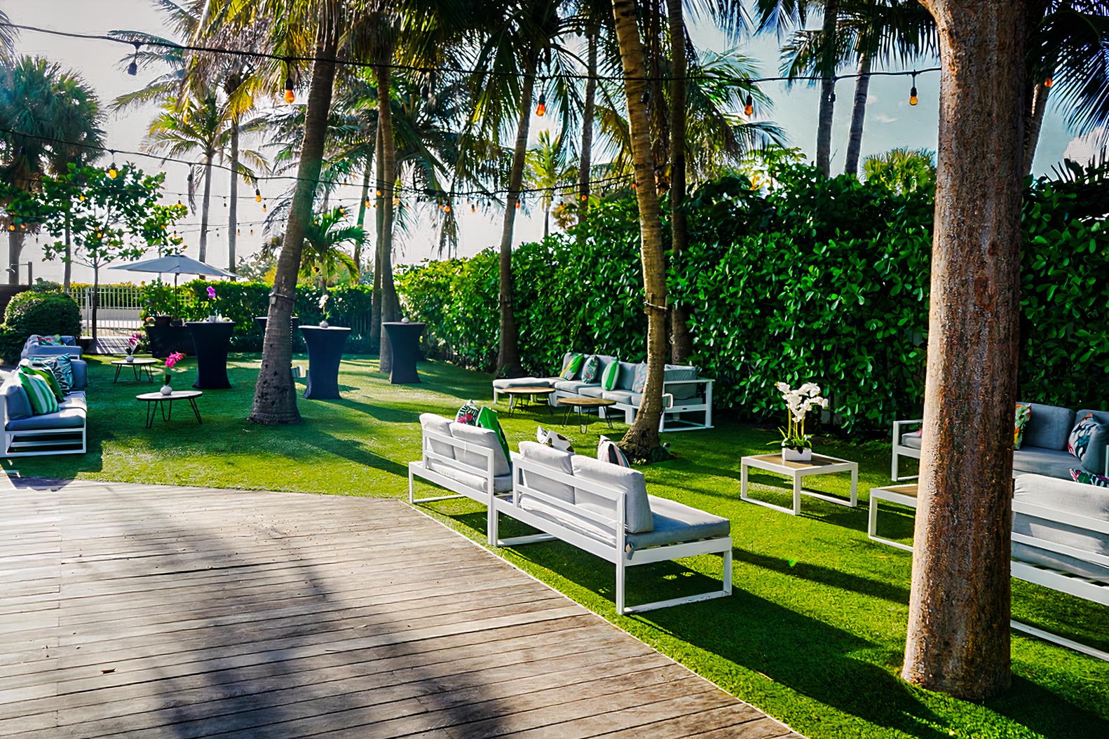 An outdoor event space with white lounge seating, palm trees, and string lights at The Marseilles Hotel.