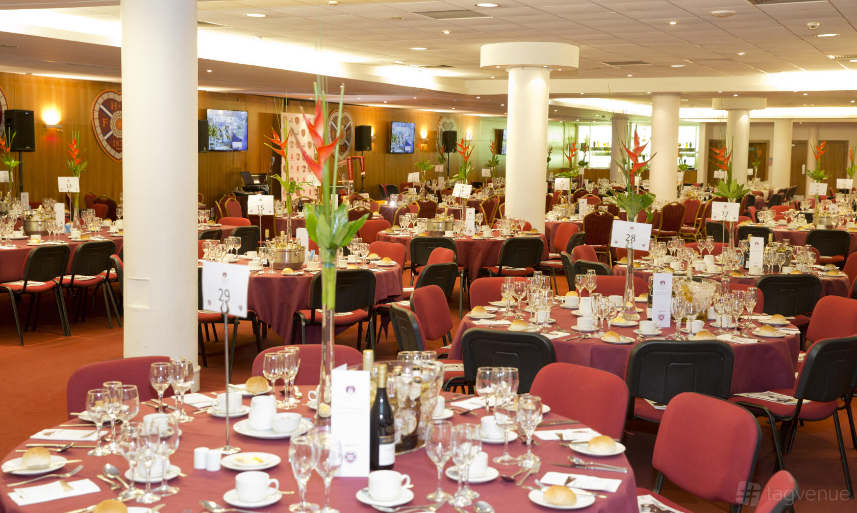 An event space with round tables covered in burgundy linens, floral centerpieces, and banquet chairs at Tynecastle Park.