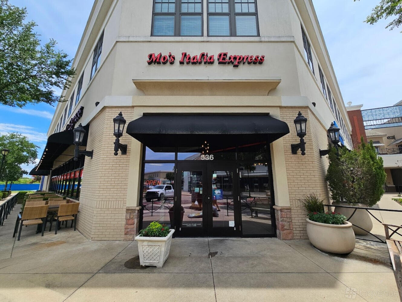 A restaurant with a black awning, outdoor seating, and glass entrance at Mo's Italia Express.