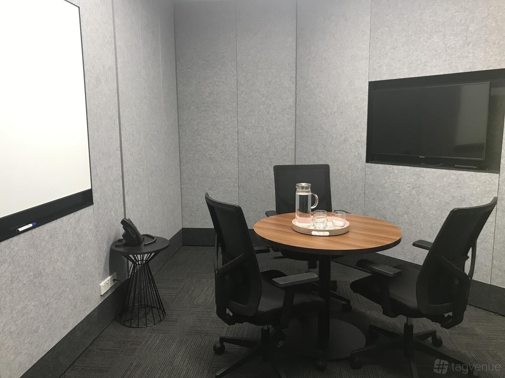 A coworking space meeting room with a round wooden table, black chairs, wall-mounted screen, and whiteboard at Compass Offices - 207 Kent Street.
