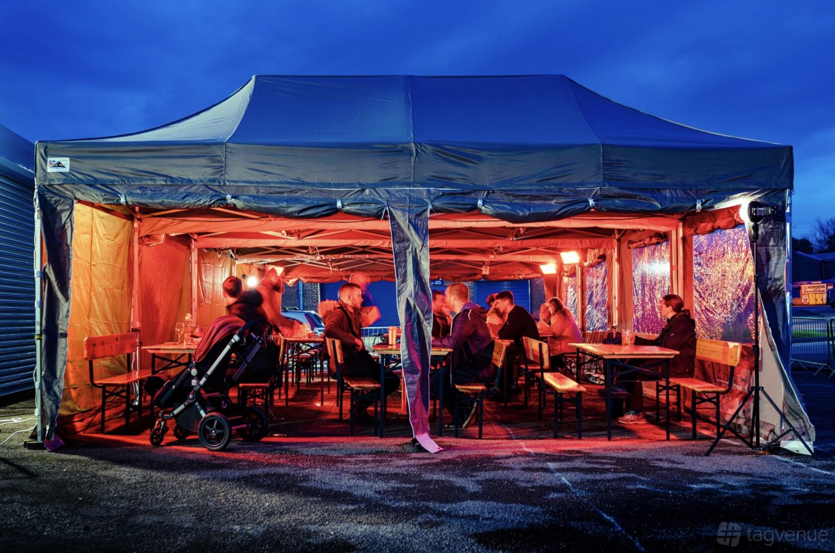 An outdoor space with long wooden tables under a large canopy tent and warm string lighting at Birmingham Brewing Company.