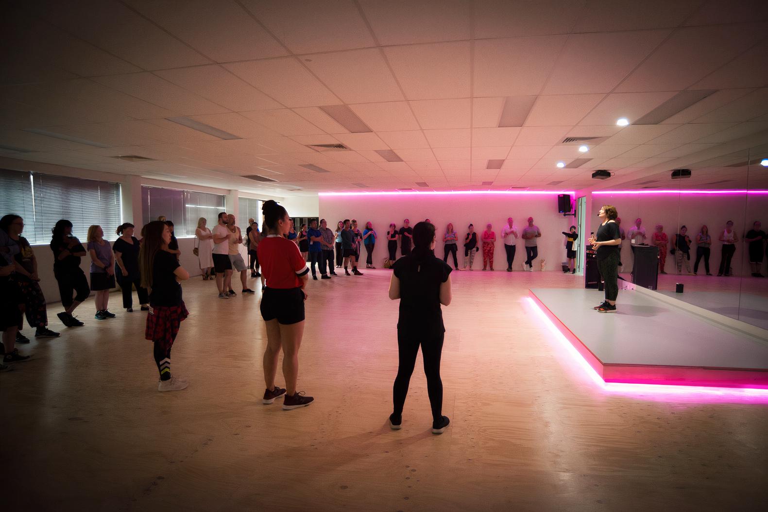 A rehearsal room with mirrored walls, wooden floors, and pink LED lighting at Glow Dance.