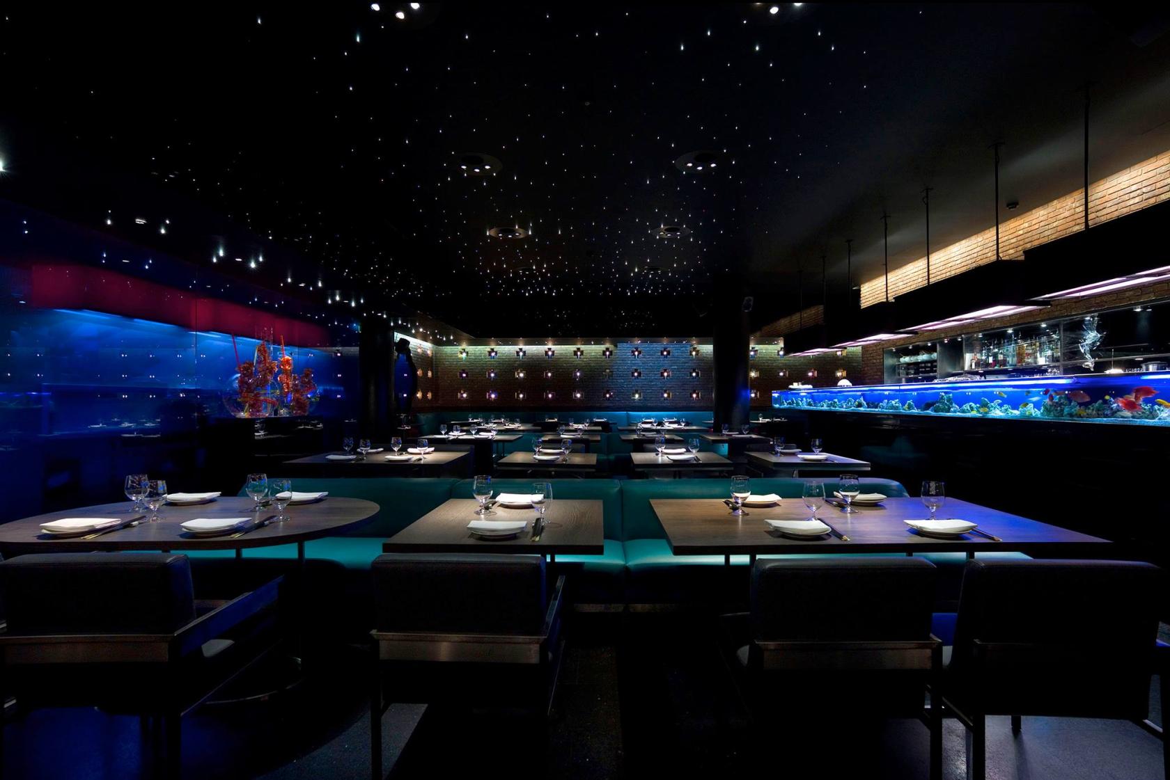 A dining room with star-like ceiling lights, blue banquettes, and a large aquarium at Yauatcha Soho.