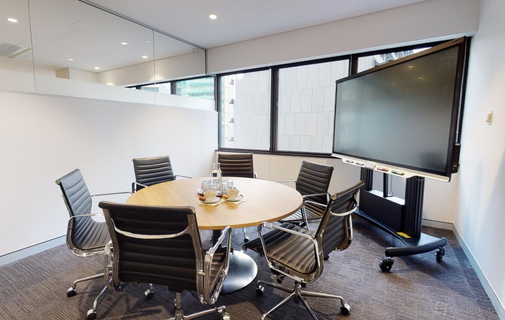 A meeting room with six black chairs around a round table, large windows, and a rolling screen at Workspace365 Bond Sydney.