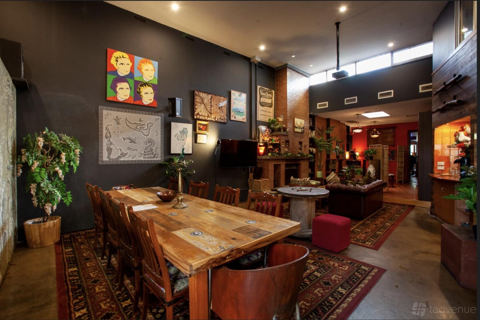 A dining room in a bar with a long wooden table, patterned rugs, eclectic wall art, and potted plants at The King of Tonga.