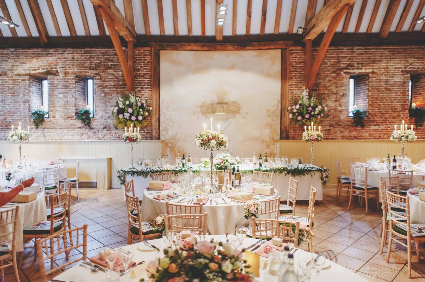 A barn venue with exposed brick walls, timber beams, round tables with floral centerpieces at Elms Barn.