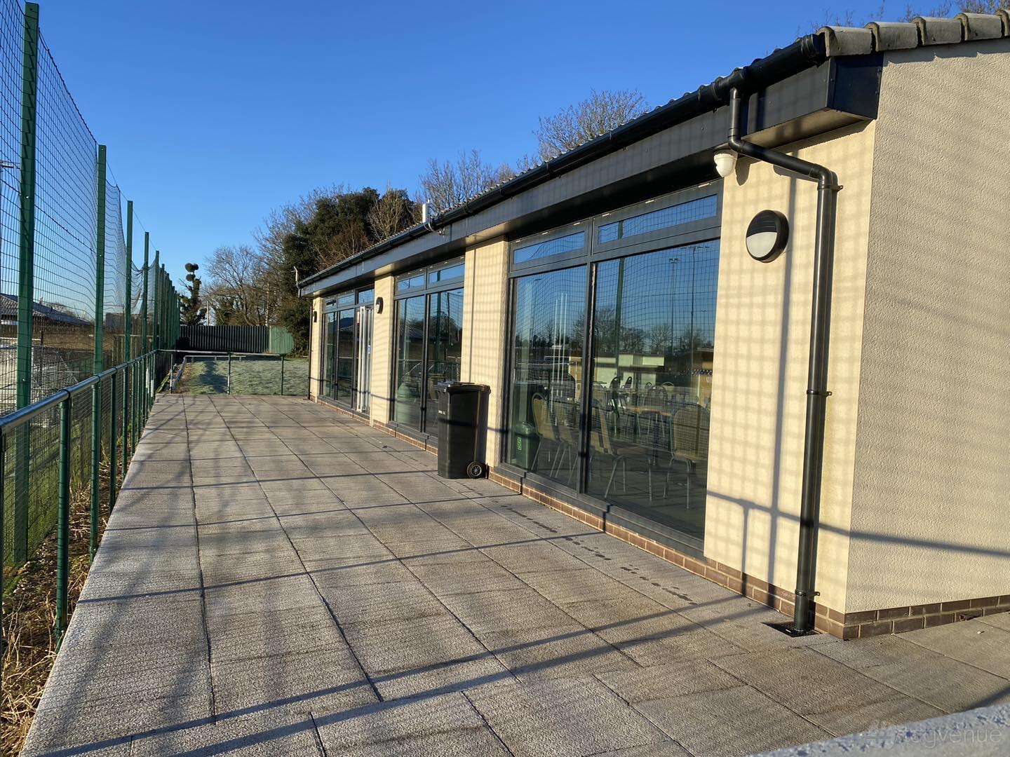 A pub with large glass windows and a paved outdoor terrace next to a sports court at Almondsbury Creative.