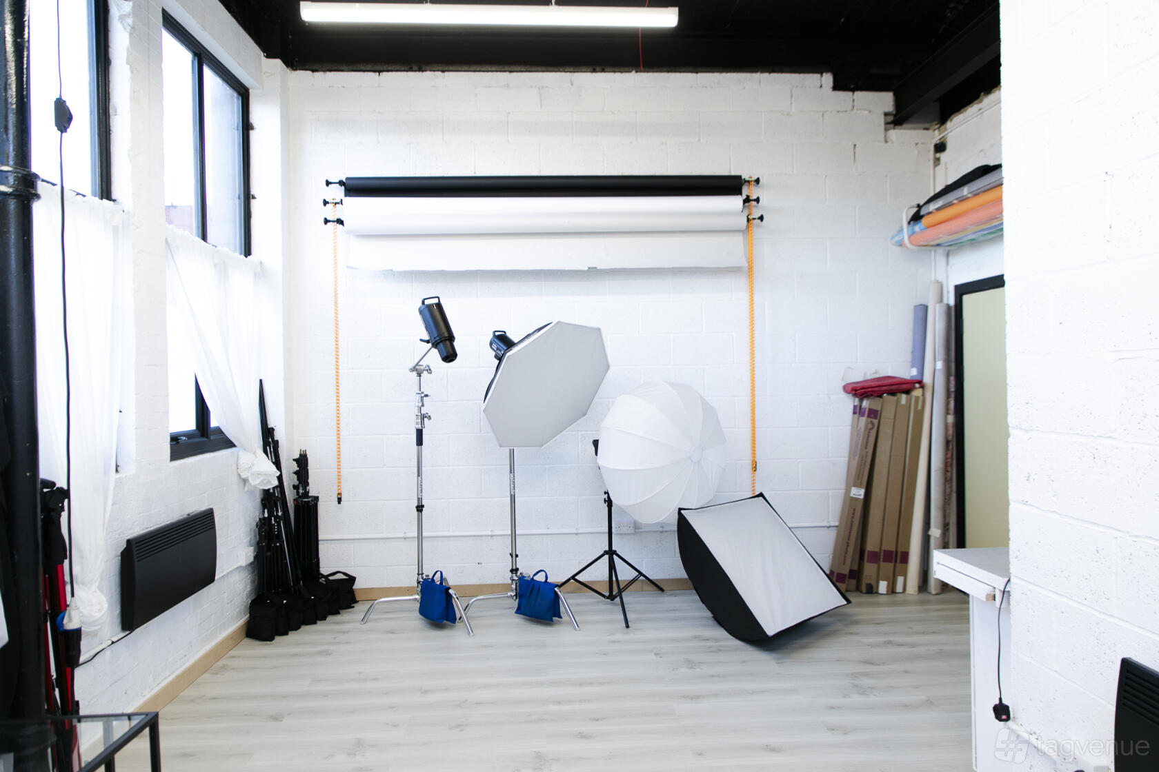 A photo studio with natural light, white walls, light wood floors, and professional lighting equipment at Studio LivMorr.