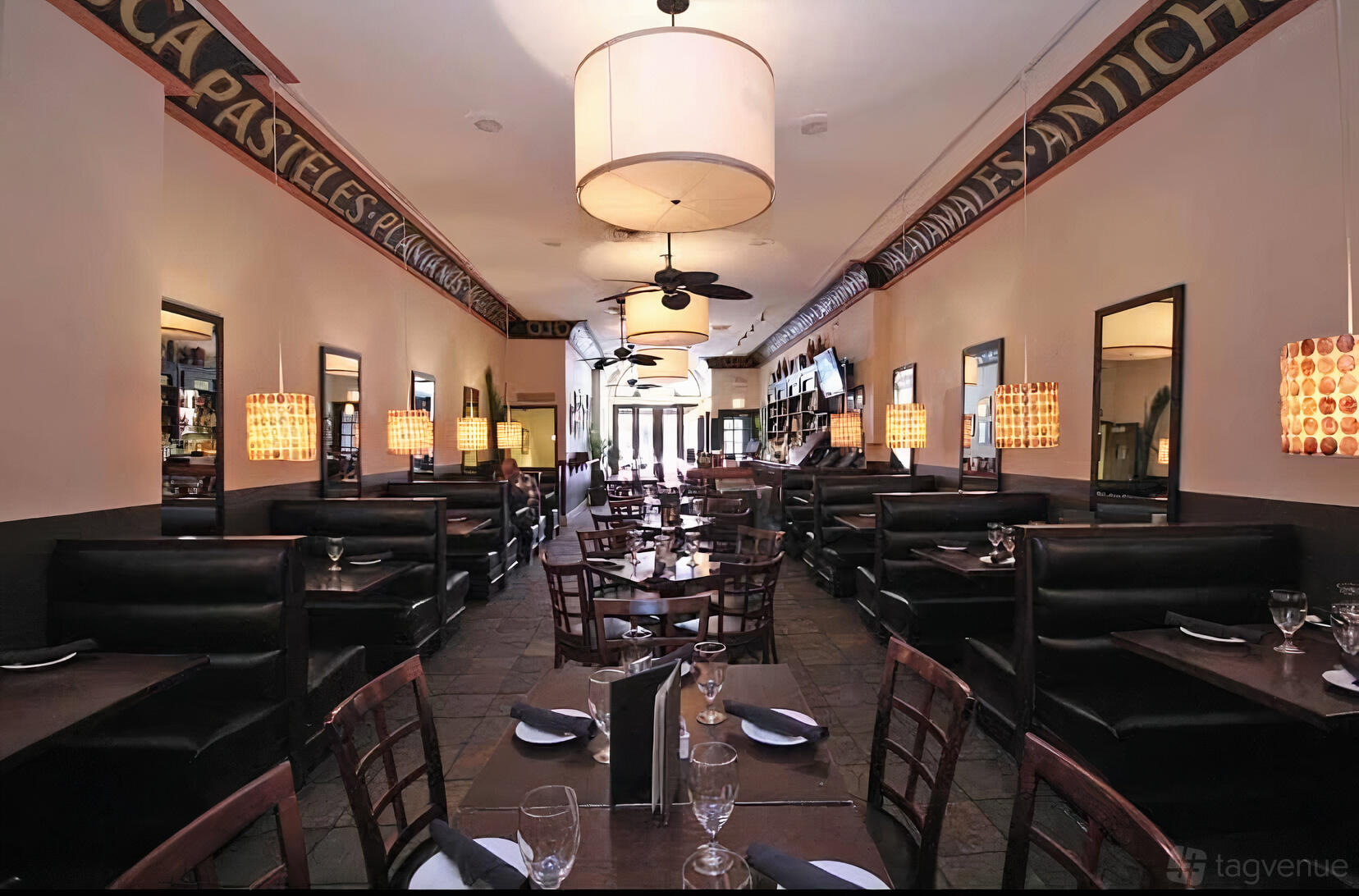 A dining room with dark wood tables, booth seating, pendant lights, and wall mirrors at Havana Grill.