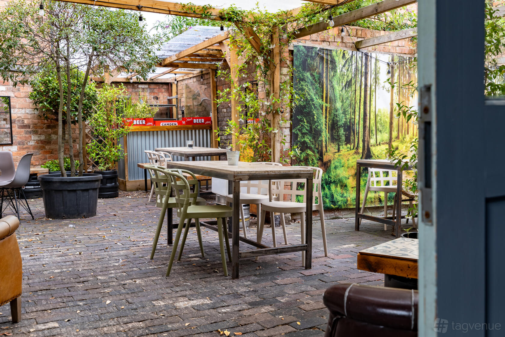 An outdoor courtyard with brick flooring, wooden tables, potted trees, and a beer bar at Temper and Brown.