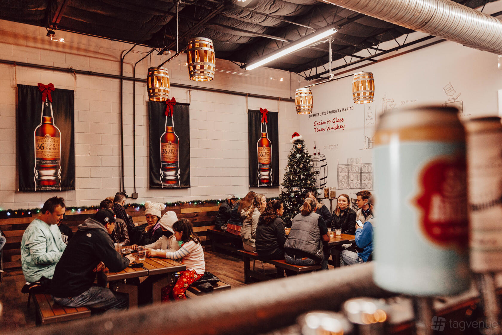 An indoor brewery event space with long wooden tables, hanging barrel lights, and festive holiday decor at Ranger Creek Brewing & Distilling.