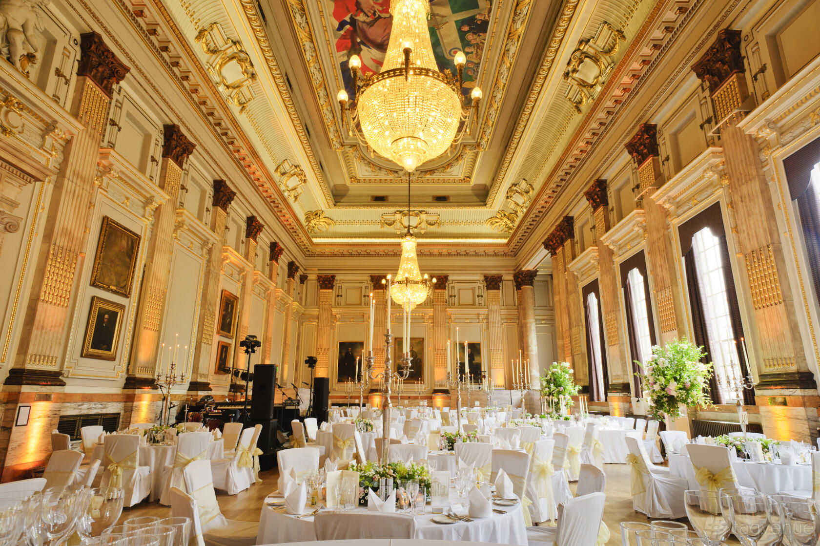 An event venue with grand chandeliers, ornate gilded columns, and round tables with white linens at One Great George Street.