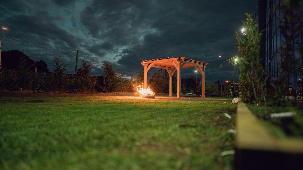 An outdoor event space with a wooden pergola and fire pit on a grassy lawn at Ultima Function Center.