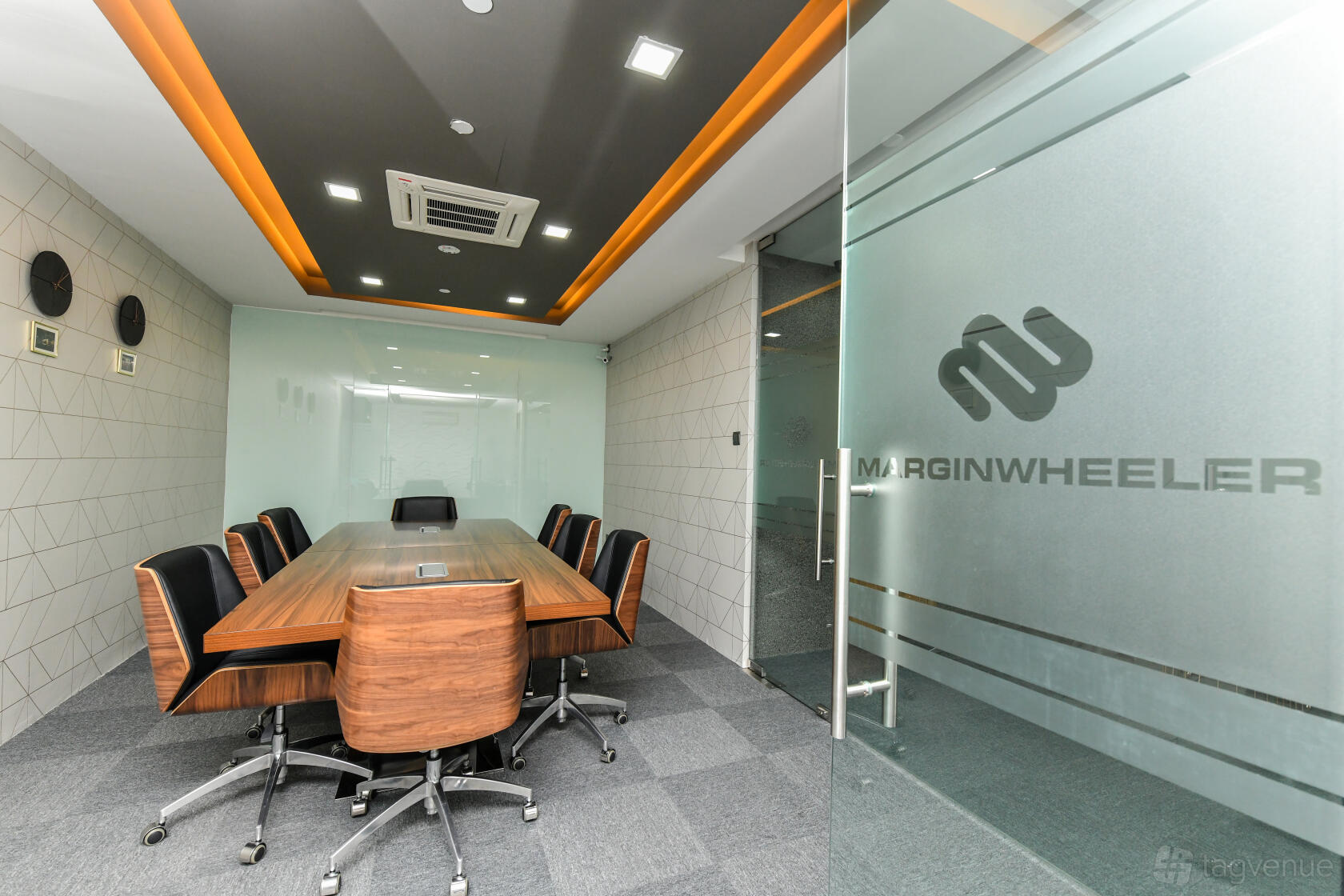 A meeting room with a long wooden conference table, ergonomic chairs, and glass walls at Wcega Tower.