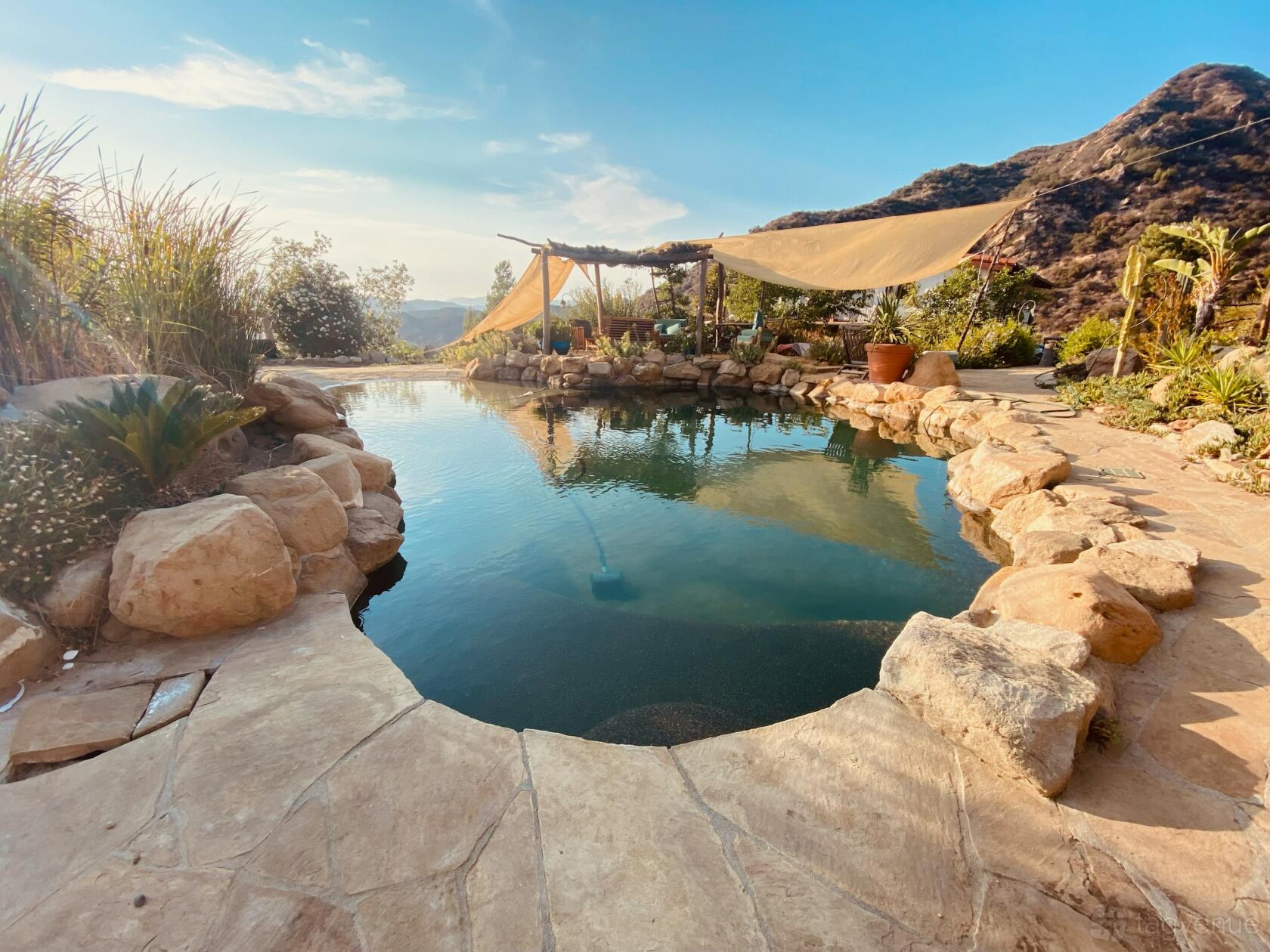 An outdoor space with a natural stone-edged pool, sail shades, and mountain views at Malibu Canyon Ranch.