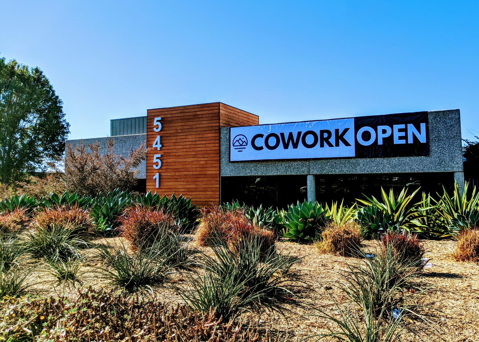 A meeting centre with a wood-paneled entrance, large street number, and landscaped garden at TrueWork Environment.