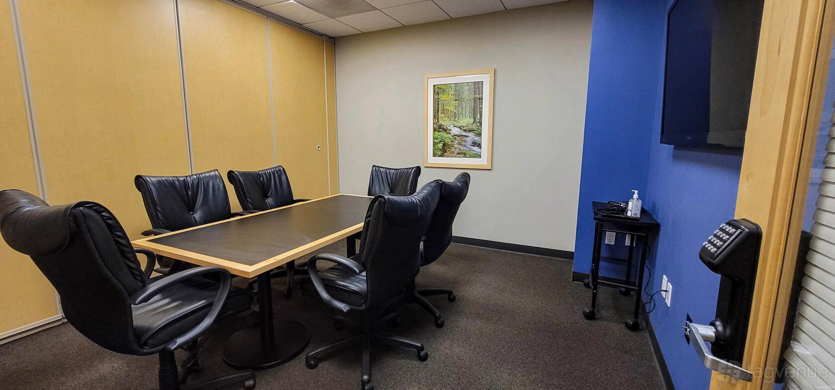 A boardroom with a rectangular table, six black leather chairs, and woodland artwork at Intelligent Office - La Jolla.
