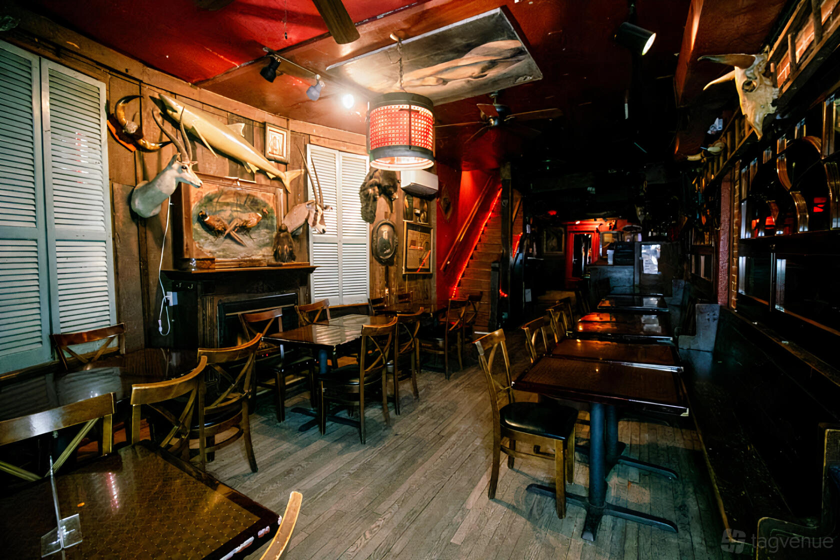 An event space in a bar with wooden tables, eclectic wall decor, and red lighting at Madam's Organ.
