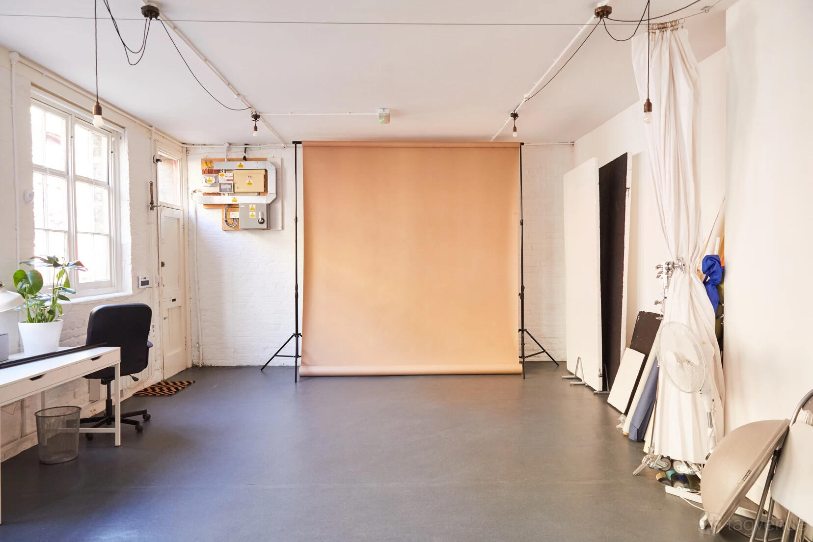 A photo studio with a beige backdrop, white walls, a desk, and natural window light at Bright Banana Studios.