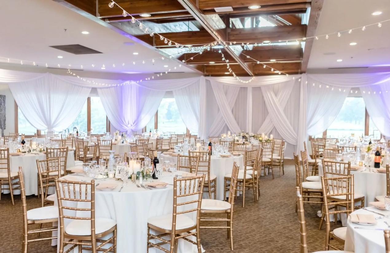 An event venue with round tables, white linens, draped walls, and skylights at Seven Bridges Golf Club.