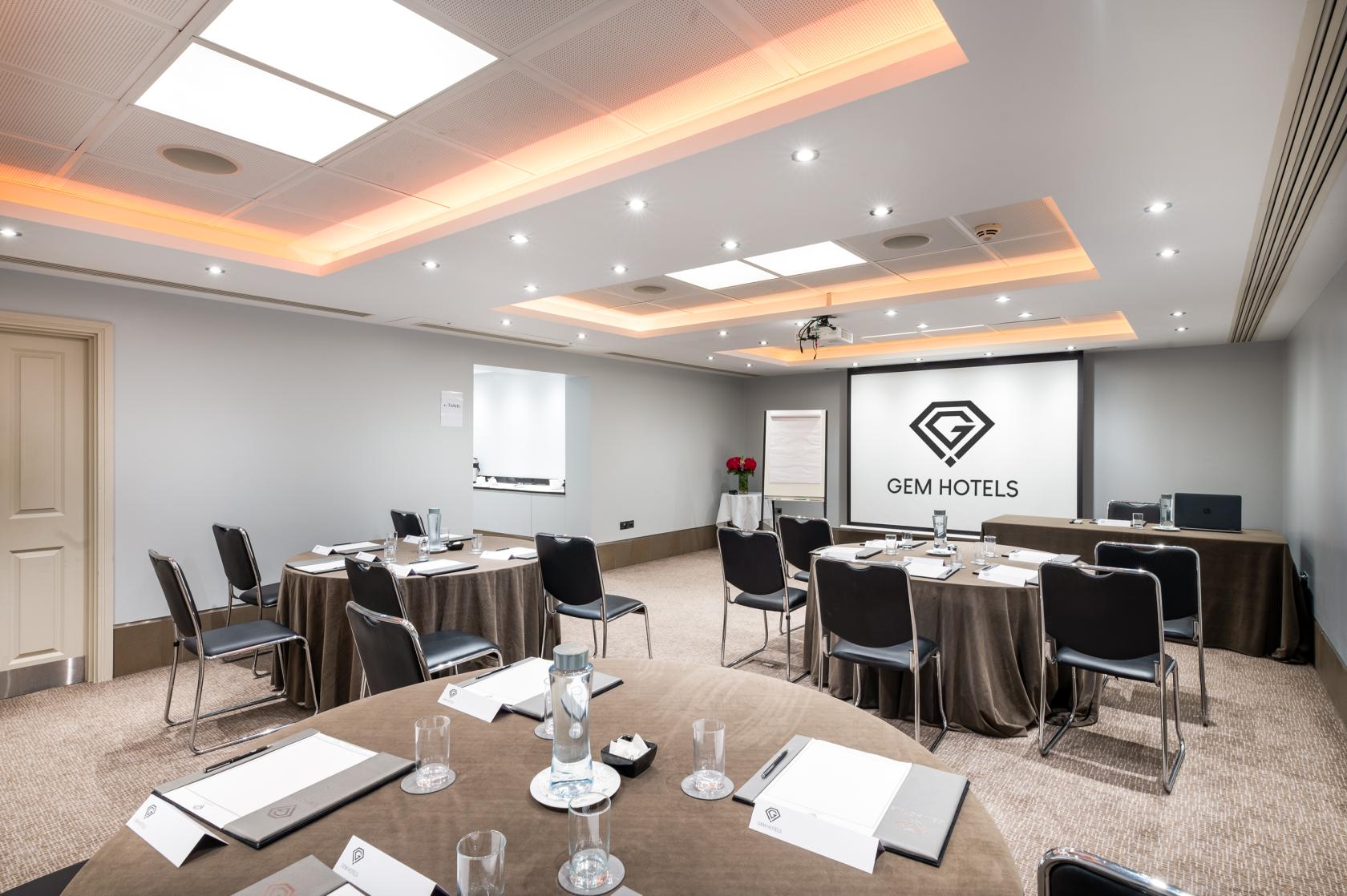 A meeting room with U-shaped tables, presentation screen, and ceiling spotlights at Langham Court.