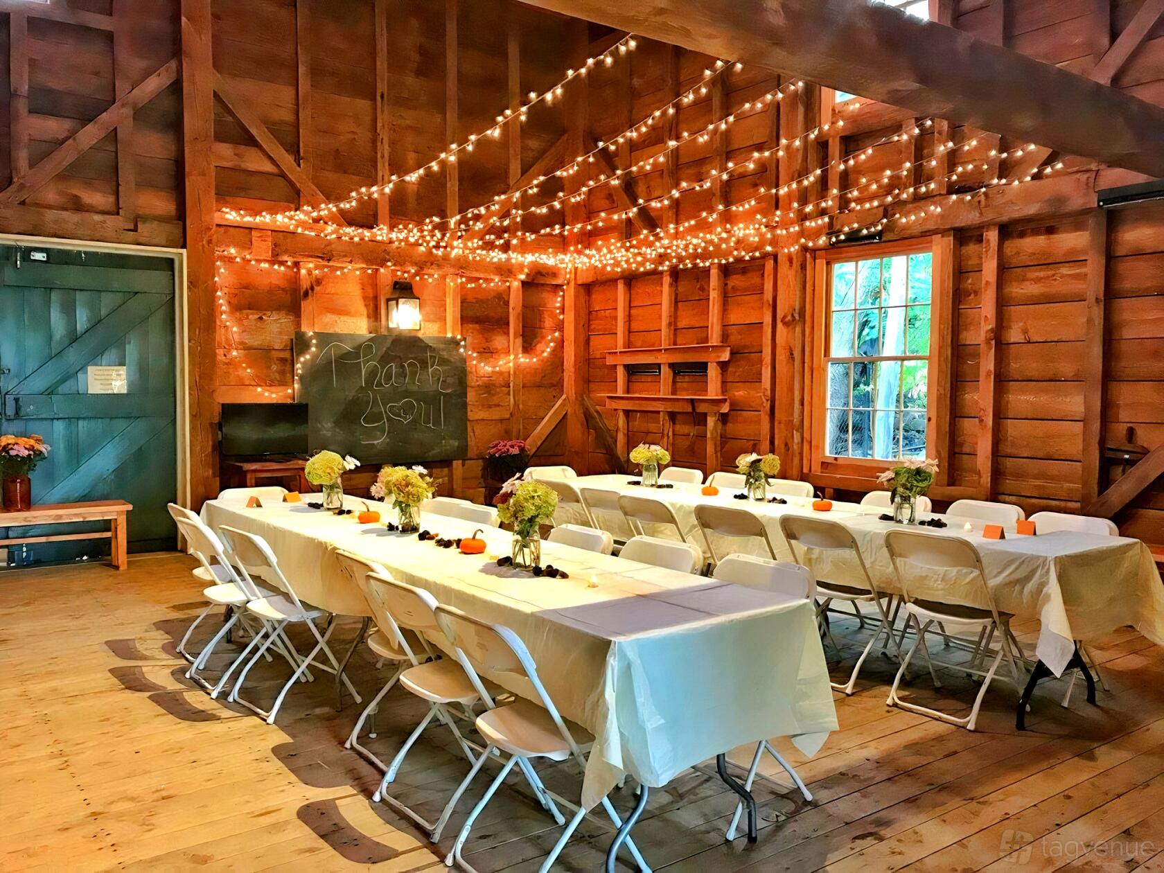 An event space in a country house with wooden walls, long banquet tables, and string lights at Shirley-Eustis House Carriage House.