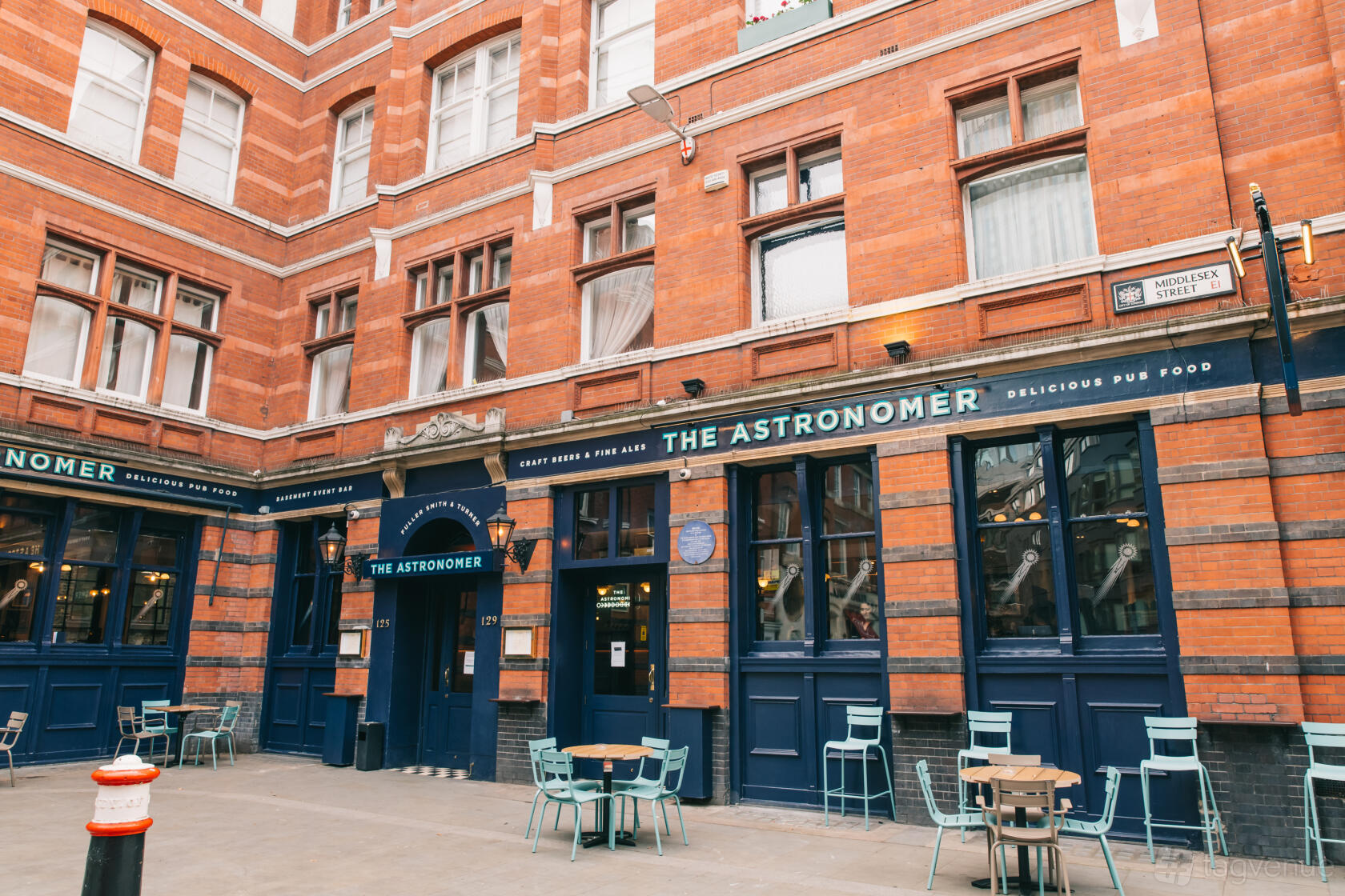 A pub with navy blue exterior, outdoor seating with small tables and chairs, and large windows at The Astronomer.