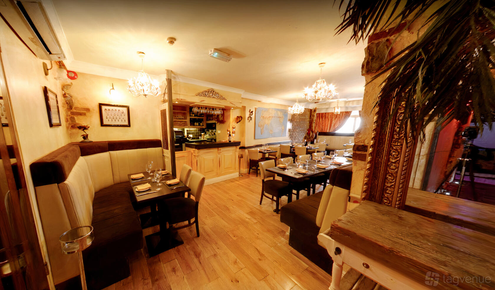 A restaurant dining room with wooden floors, upholstered booth seating, chandeliers, and set tables at Darwins Restaurant.