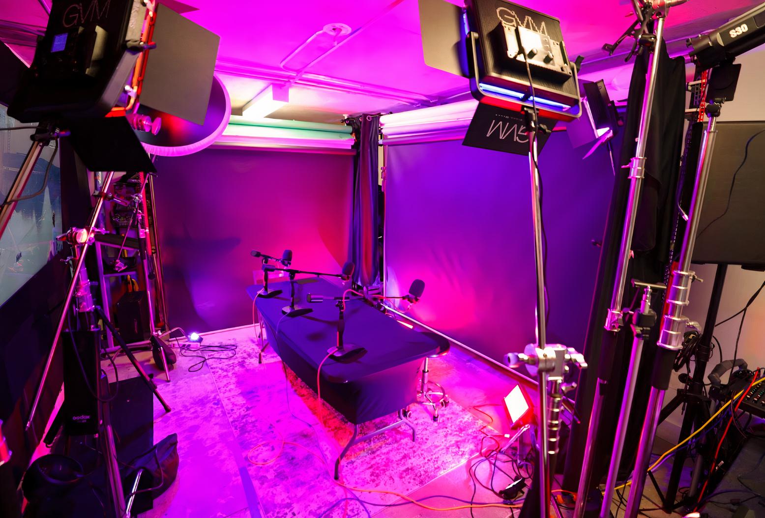 A podcast studio with neon lighting, a black table, microphones, and professional video equipment at Streetz Media.
