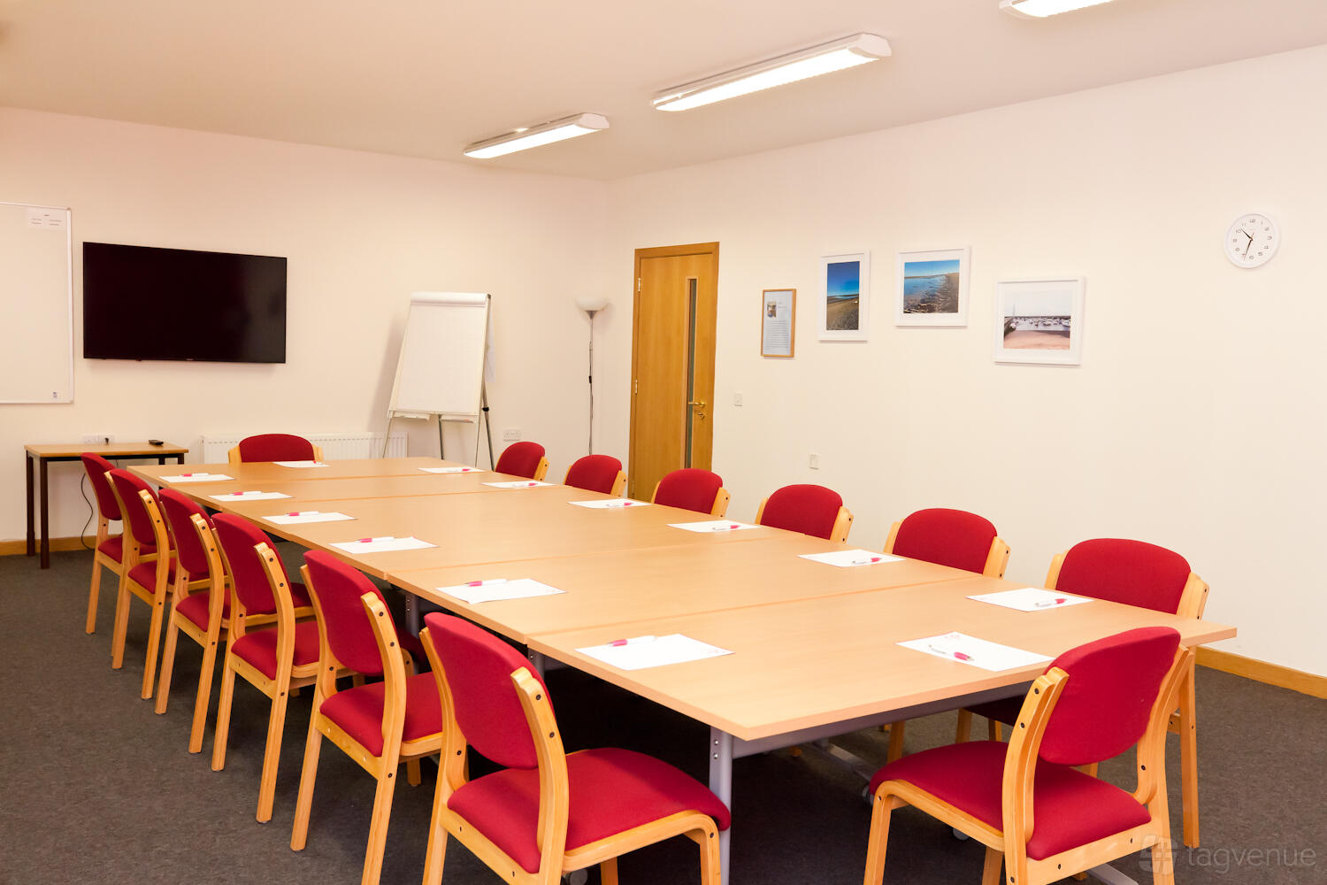 A conference centre room with a U-shaped table arrangement, red chairs, wall-mounted screen, and flip chart at Norton Park Conference Centre.