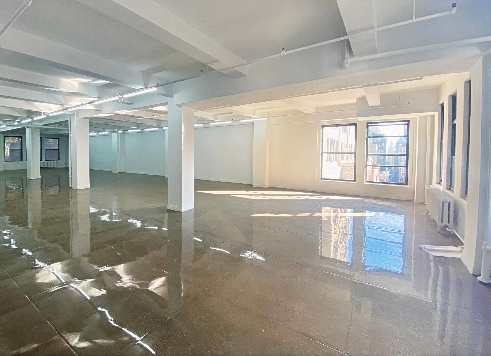 An event space with polished concrete floors, white columns, and large windows at CINEPLAY.