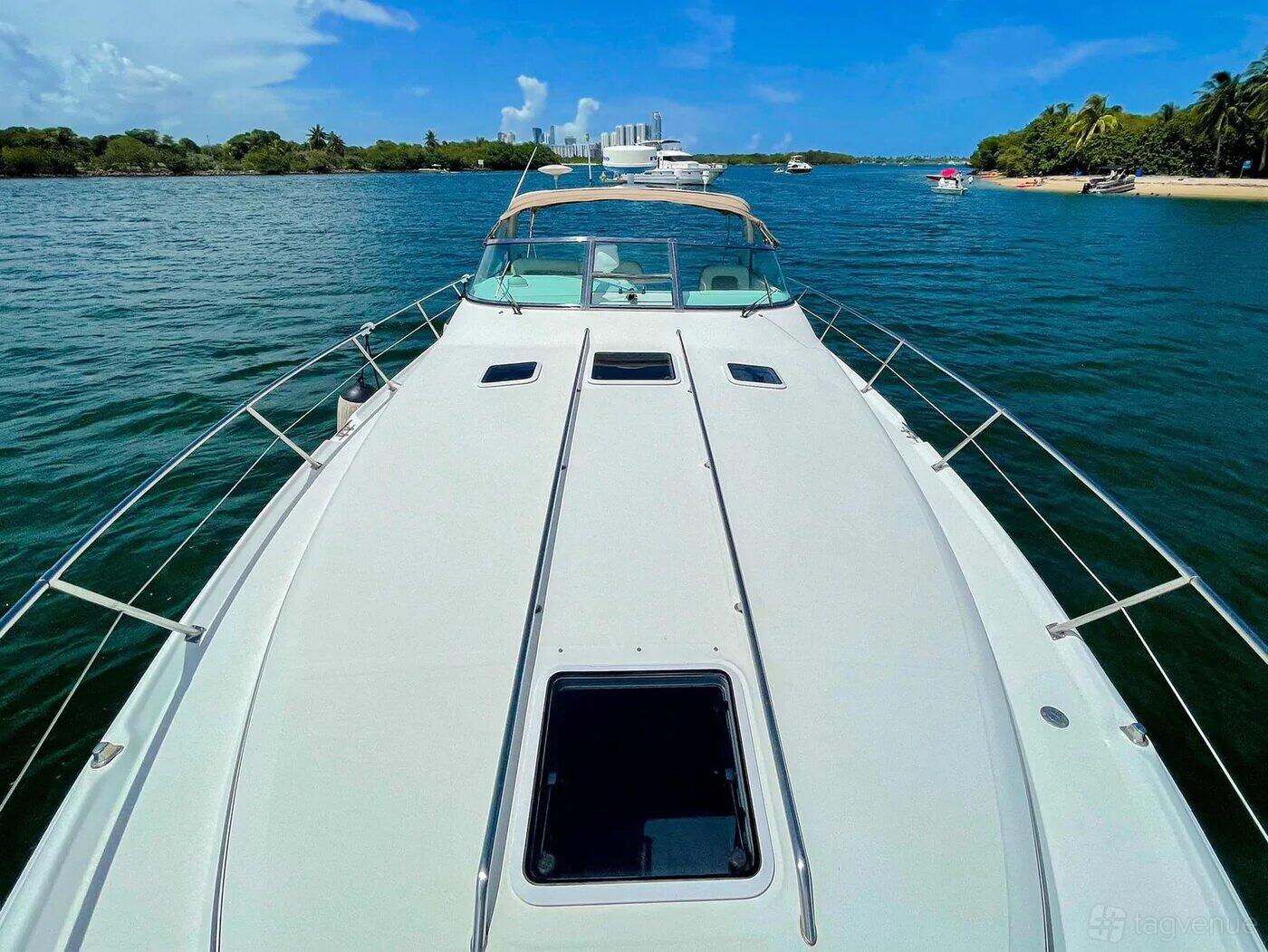 A boat deck with stainless steel railings and views of the water and shoreline at VIP Boat Rental @ Alton Road.