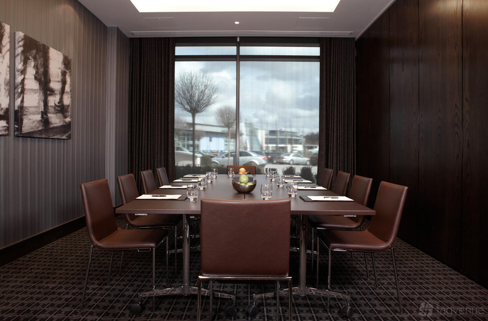 A meeting room with a large window, brown leather chairs, and a conference table set for twelve at Brooklands Hotel.