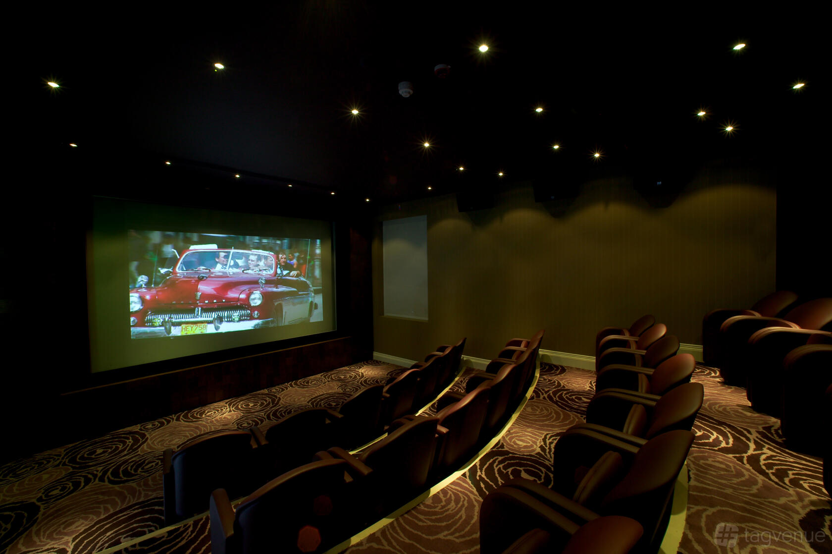 A cinema with tiered rows of cushioned seats, patterned carpet, and a large projection screen at The Roseate Reading.