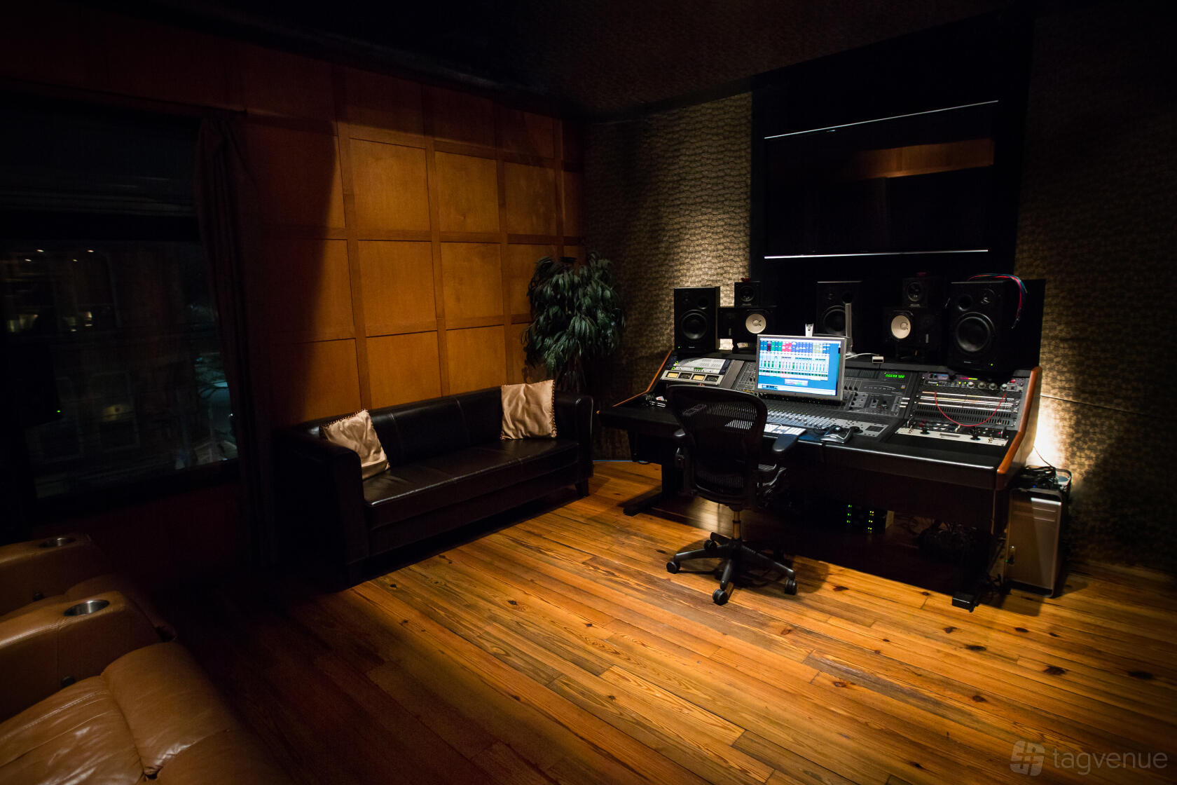 A music studio with a mixing console, studio monitors, wood floors, and a black leather sofa at The Orange Lounge.