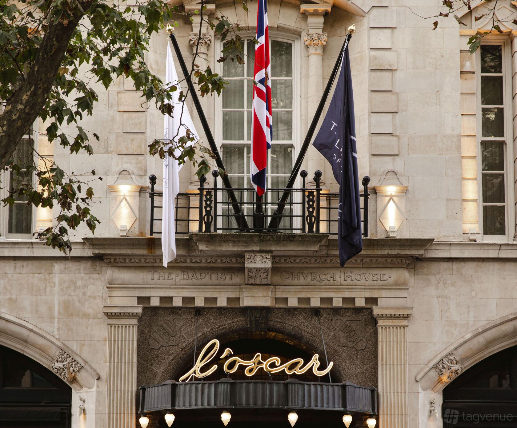 A hotel entrance with stone archways, flagpoles, and illuminated signage at L'oscar London
