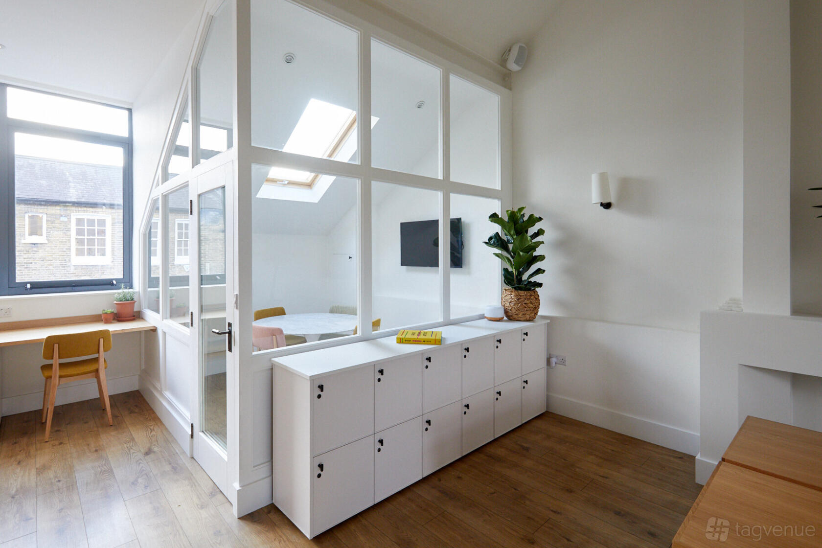 A meeting room with glass walls, skylight, built-in lockers, and a wall-mounted TV at The Hearth.