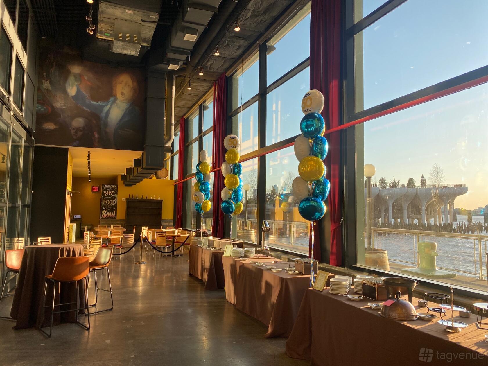 A dining room with floor-to-ceiling windows, buffet tables, and colorful balloons at City Winery.