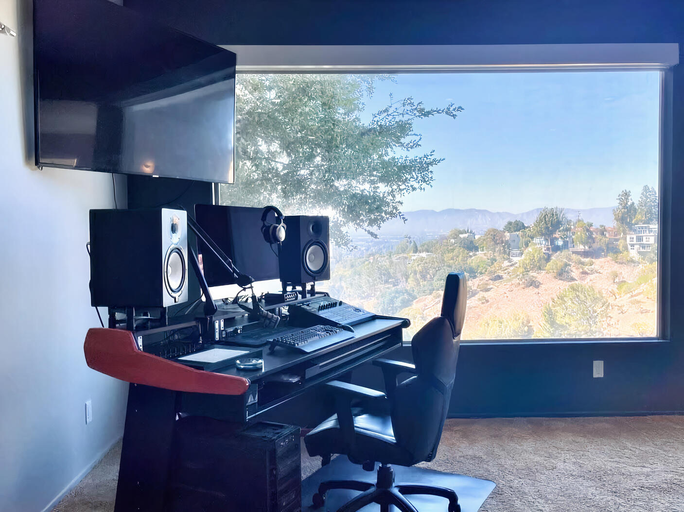 A recording studio with dual monitors, speakers, and a large picture window overlooking the hills at Private Hollywood Hills Mansion.