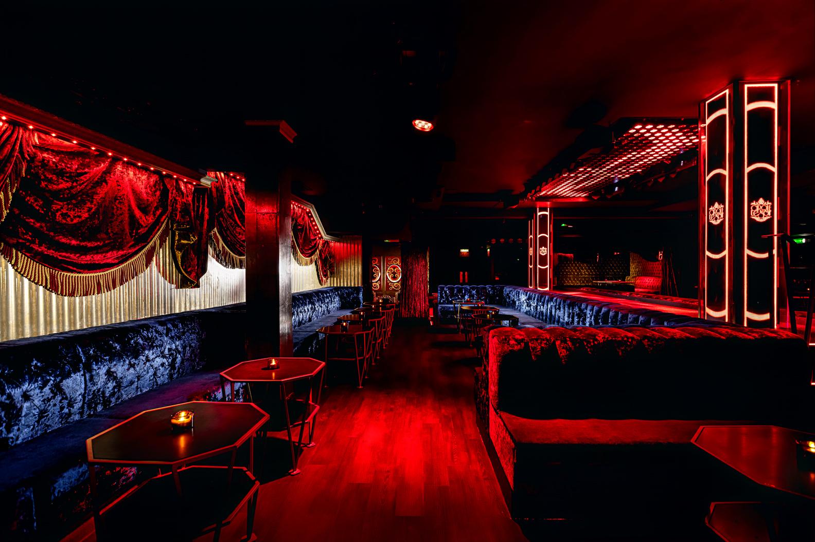 A nightclub event space with plush velvet seating, red lighting, and gold draped curtains at Cirque le Soir.