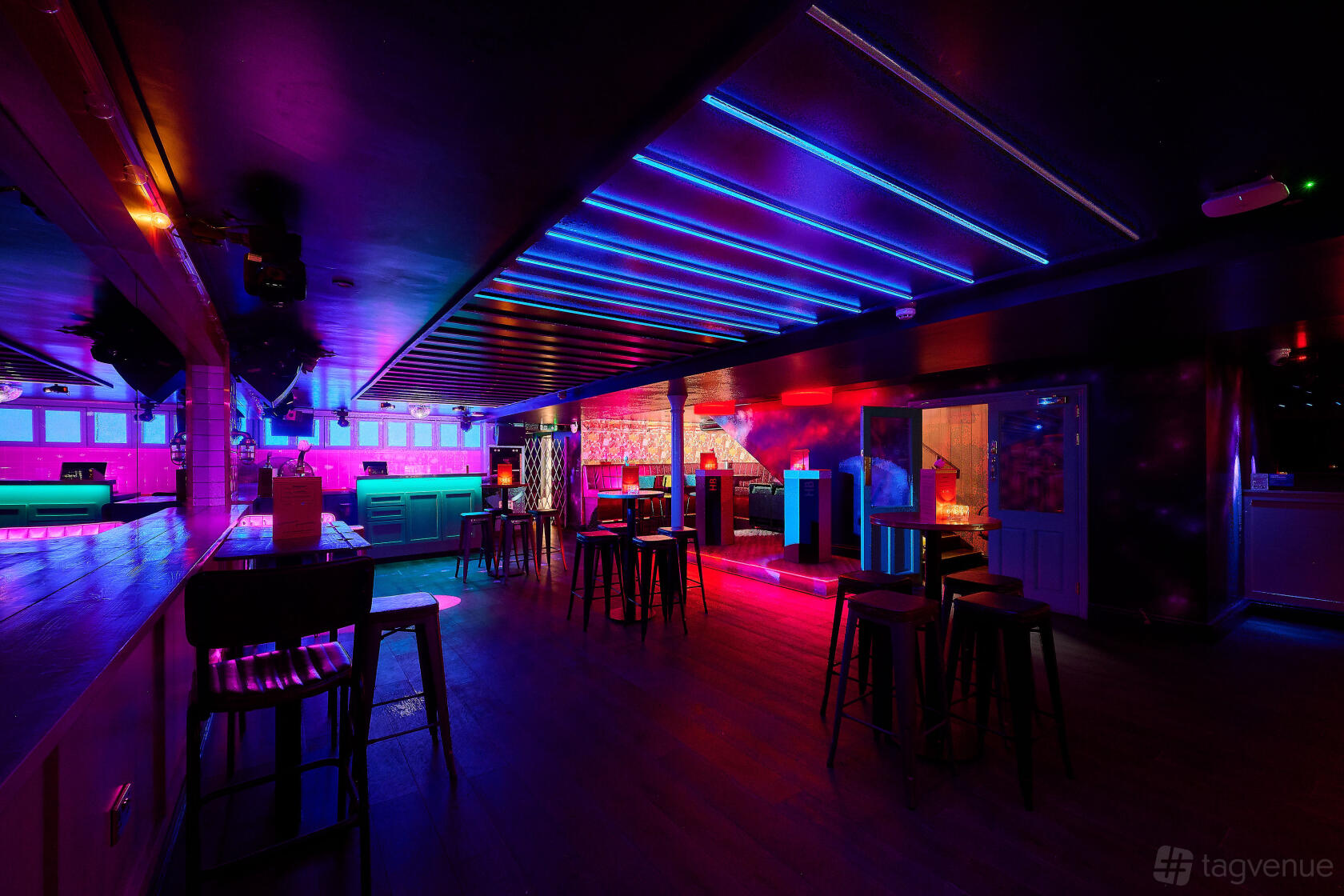 A function room in a cocktail bar with neon lighting, high tables, bar seating, and a dance floor at Simmons | Shoreditch.